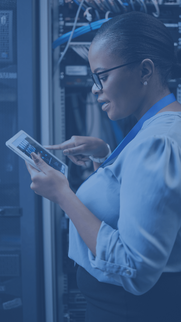 Female data analyst standing in front of server with a tablet, analyzing data.