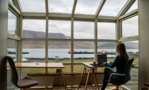 Women working on laptop in front of backdrop of mountains and water. Remote working - Insider Risk Travel Tips